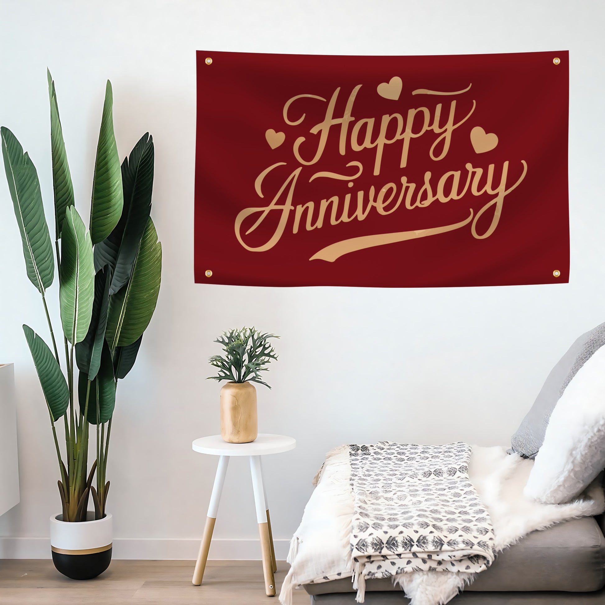Red flag banner with 'Happy Anniversary' text hanging on a wall above a sofa with decorative plants.