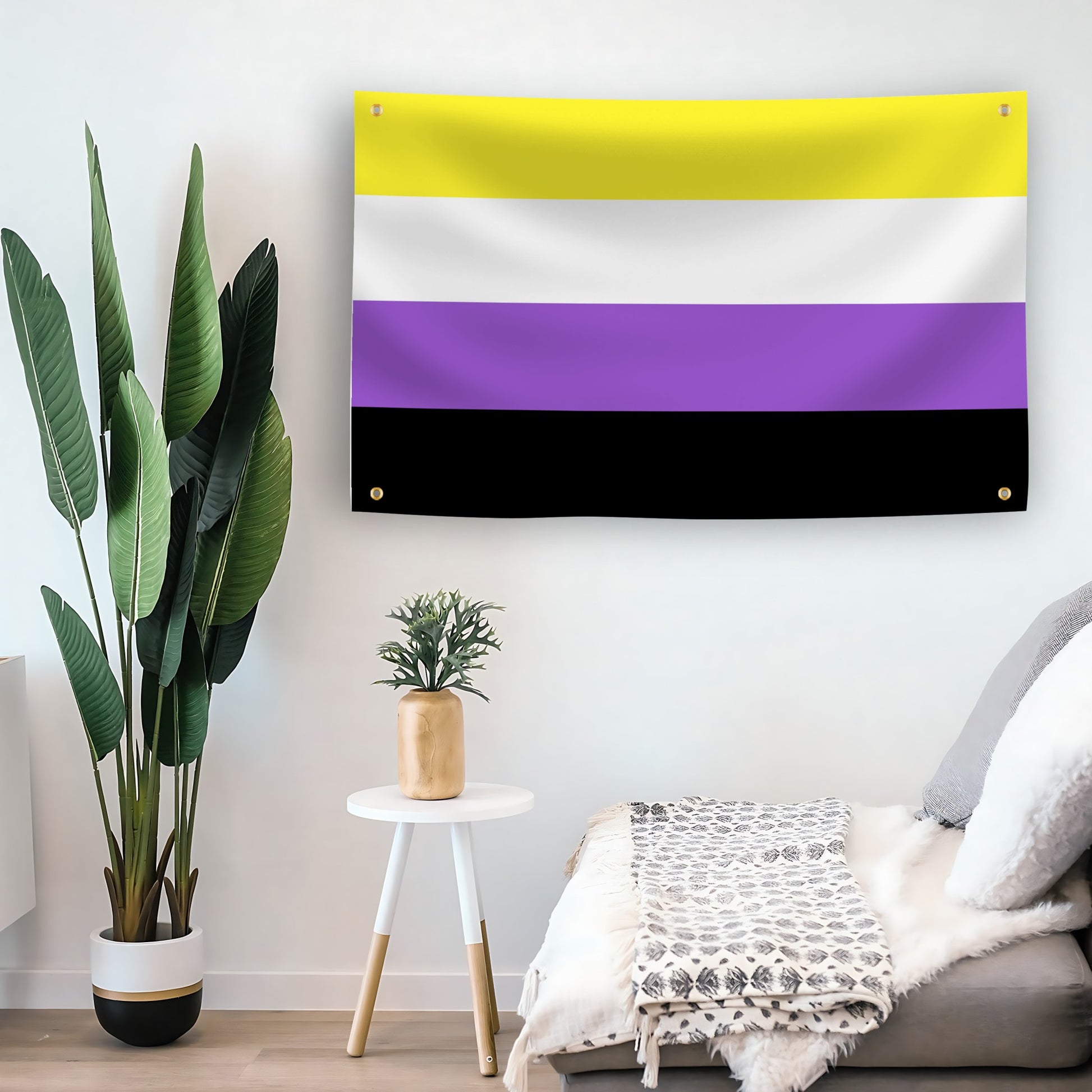 The nonbinary pride flag hanging on the wall in a living room with a plant, small table, and couch