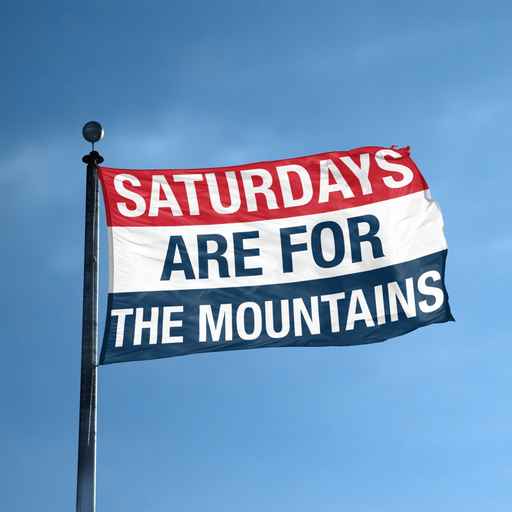 Flag with 'Saturdays are for the Mountains' text against a blue sky