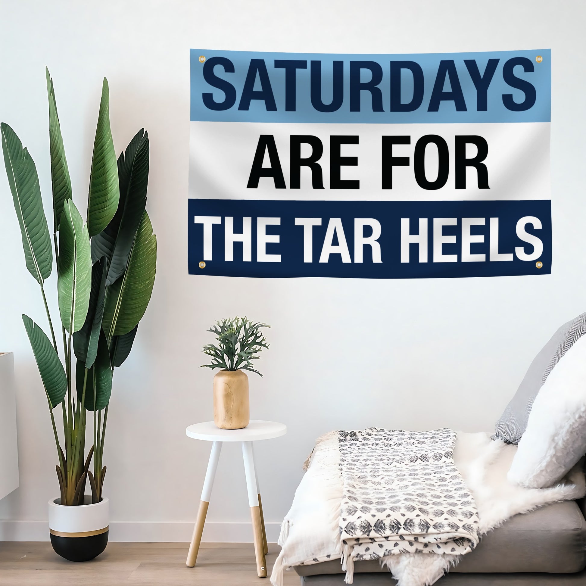 A flag banner with a blue and white color scheme, featuring the text 'SATURDAYS ARE FOR THE TAR HEELS' in bold letters mounted on a wall. 