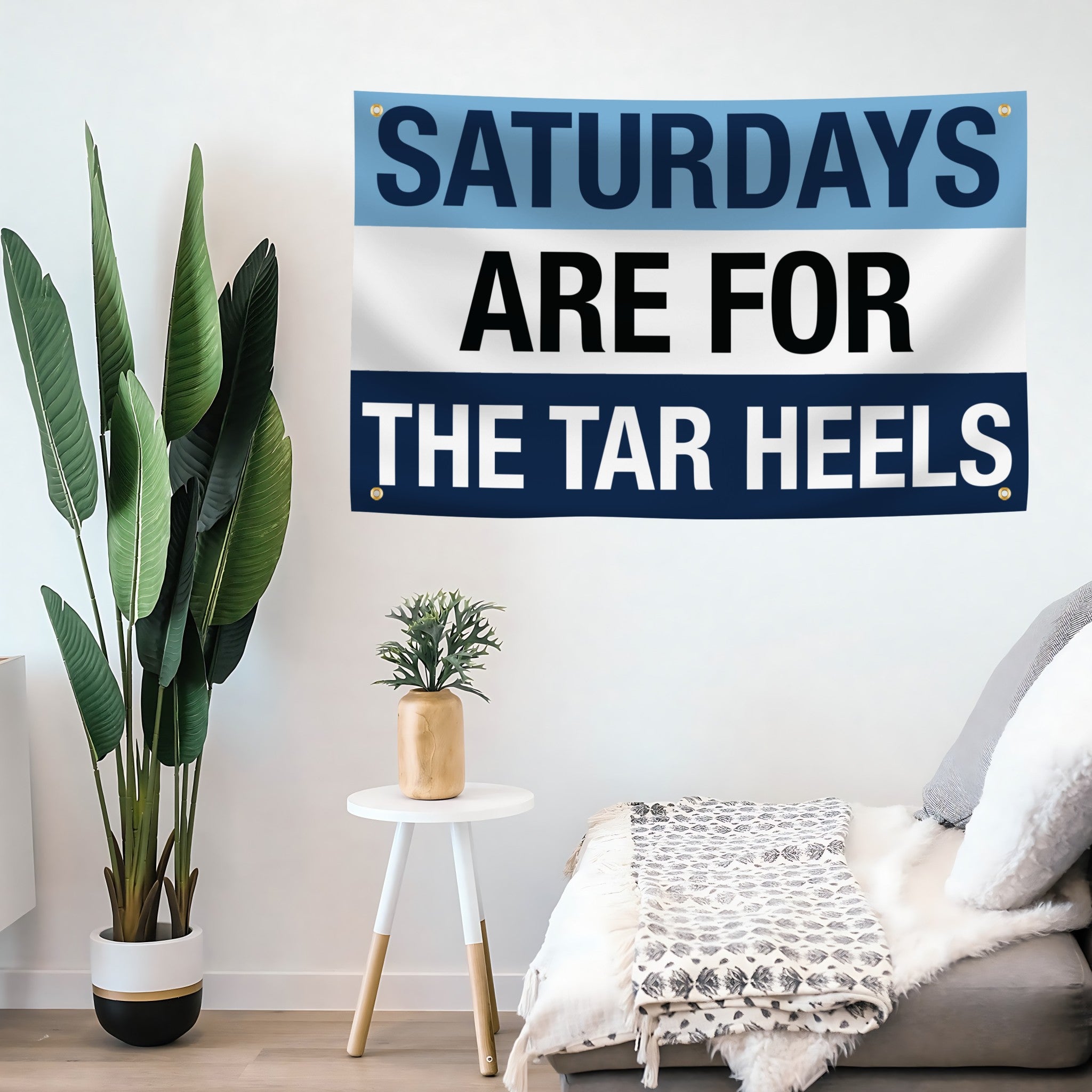 A flag banner with a blue and white color scheme, featuring the text 'SATURDAYS ARE FOR THE TAR HEELS' in bold letters mounted on a wall. 