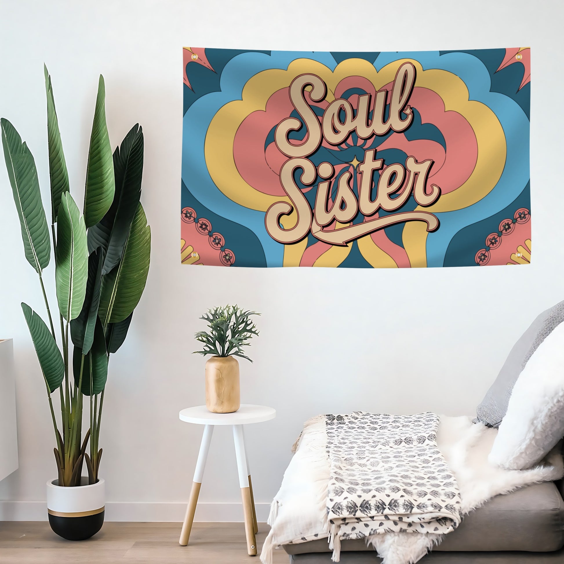 Colorful 'Soul Sister' flag banner on a wall with plants and a chair in the foreground.