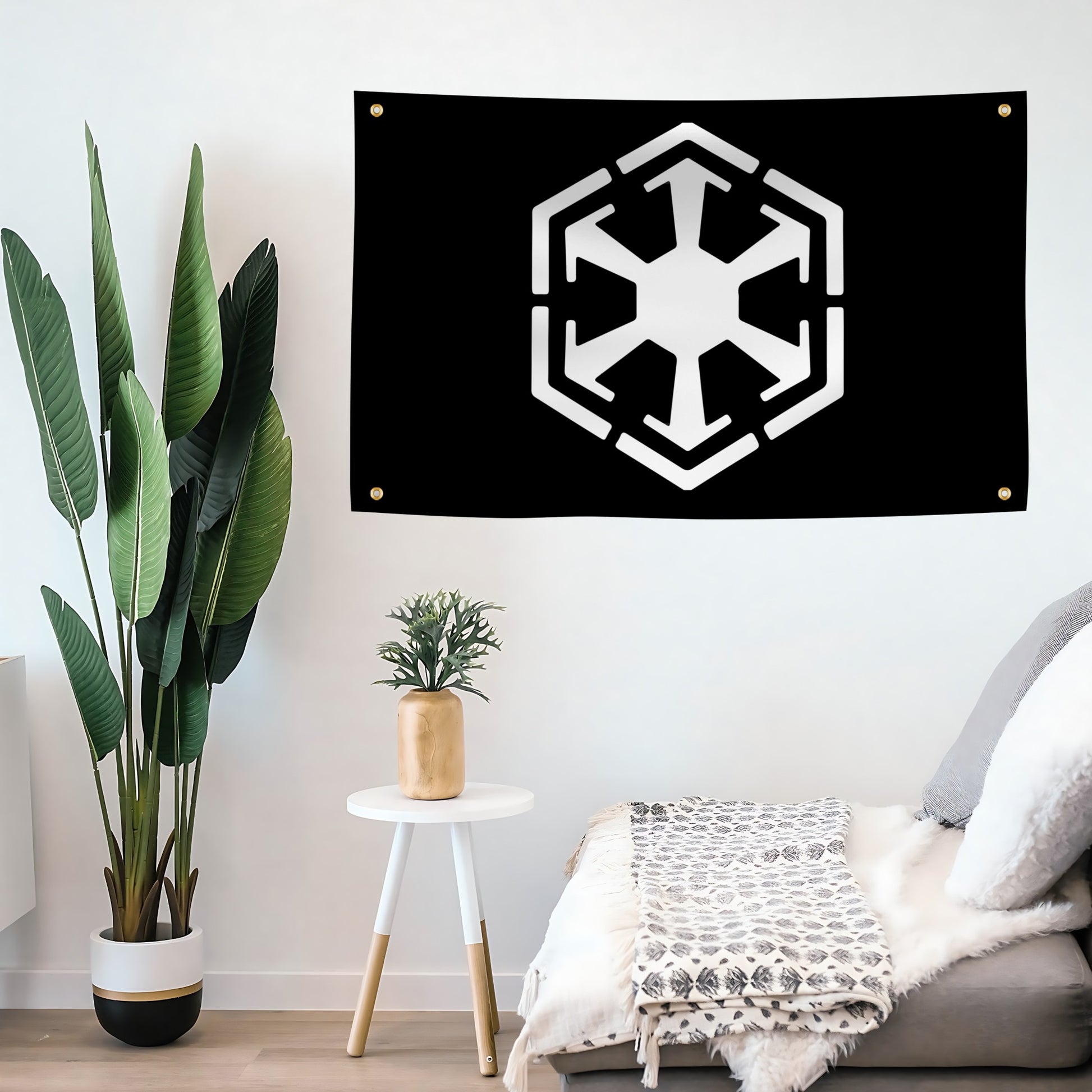 A black wall banner featuring the white Star Wars Sith Empire symbol, hanging on a white wall in a styled bedroom setting with a plant, side table, and bed.