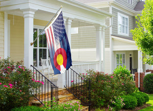 an american and colorado flag on a flagpole in front of a house